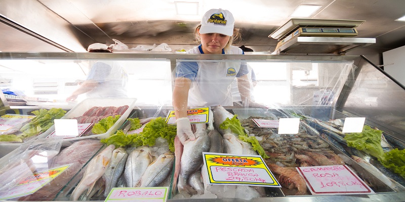 Microempreendora de avental, luva e boné brancos organiza peixes de sua venda.