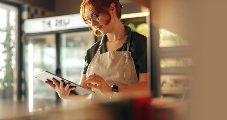 Mulher de avental usando um tablet dentro de um café.