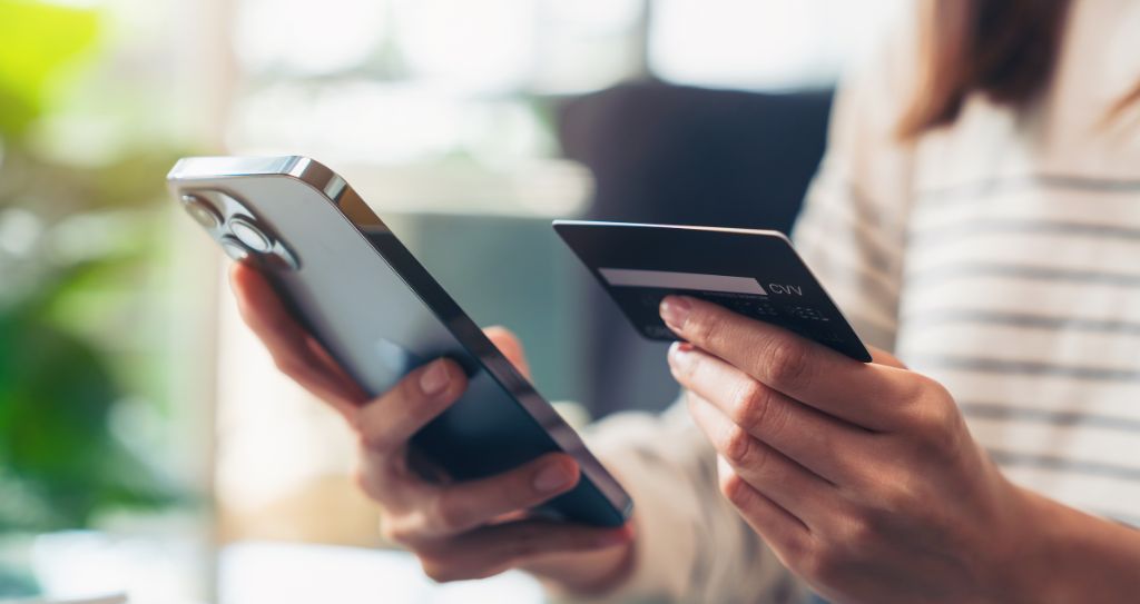 Pessoa segura um smartphone e um cartão de crédito, potencialmente utilizando esse meio de pagamento em compras online.