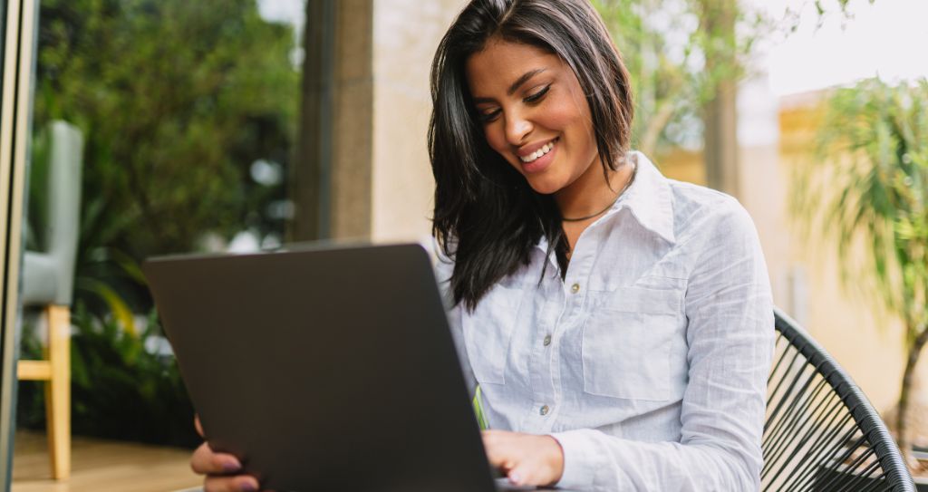 Mulher empreendedora de cabelos lisos trabalhando em notebook ao ar livre, mostrando a atuação do empreendedorismo feminino no ambiente digital com as soluções Cielo.