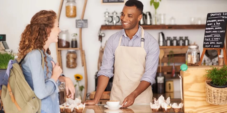 Empreendedor de avental serve café para cliente de sua loja sorrindo.