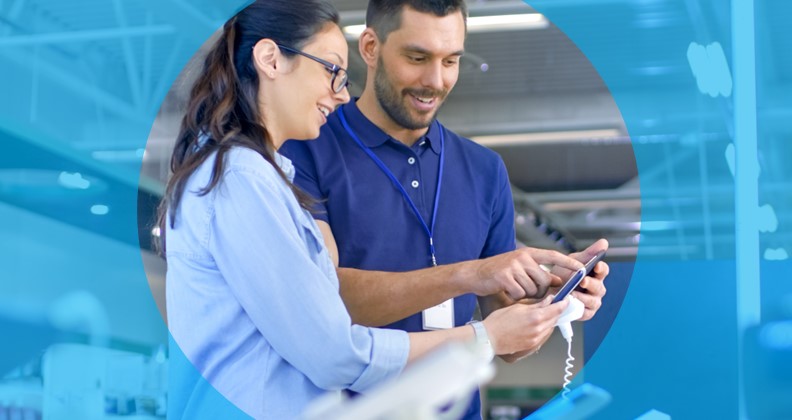 Duas pessoas em um ambiente de um dos maiores varejistas do Brasil analisam um dispositivo eletrônico móvel que está num display de vendas; uma delas aponta algo na tela enquanto conversam.