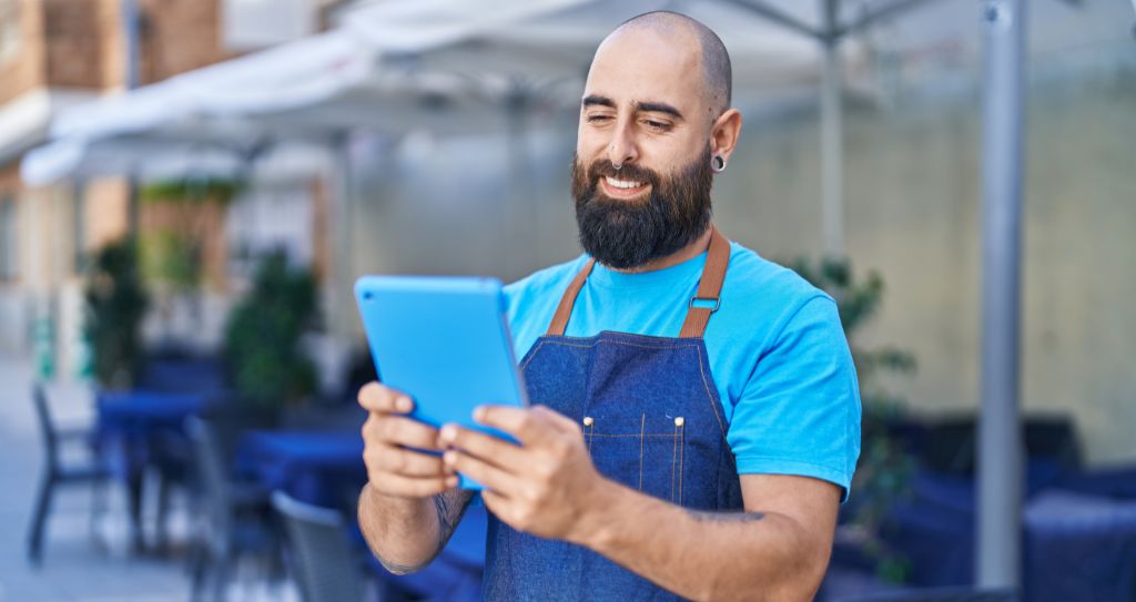 Empreendedor sorridente usando um tablet na calçada de seu negócio. Exemplo de gestão eficiente da sua loja online com o apoio de um gateway de pagamento.