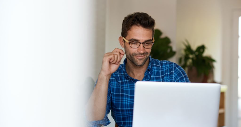 Homem de camisa xadrez azul trabalhando em um laptop em uma sala iluminada.