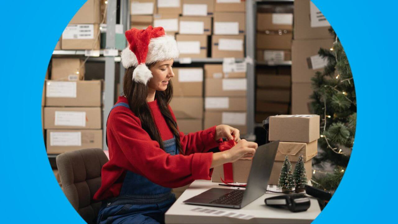 Mulher com gorro de Papai Noel embalando caixas em um estoque decorado, mostrando na prática como criar promoções de Natal focadas em logística, presentes e envio rápido.
