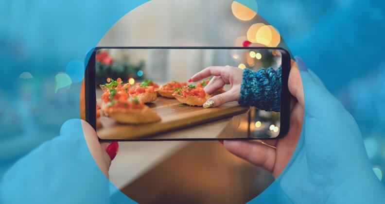 Smartphone tirando foto de comida sobre tábua de madeira para divulgar no Instagram.