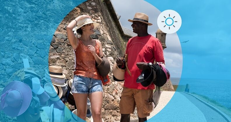 Empreendedor vende chapéu para mulher turista em rua próximo à praia na temporada de calor.