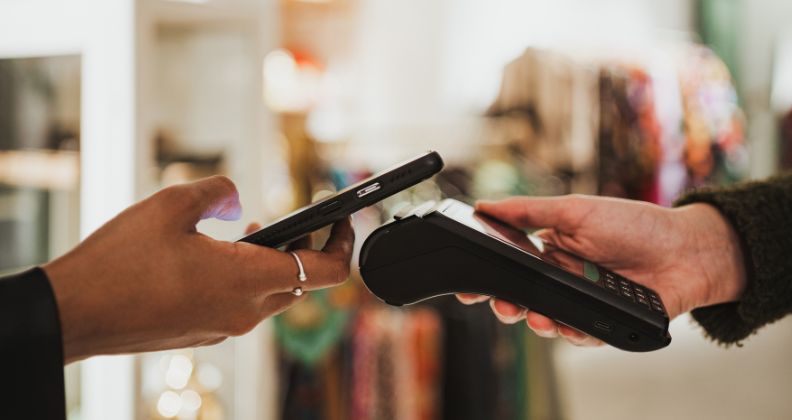 Pessoa fazendo um pagamento sem contato com um smartphone para um terminal de cartão.