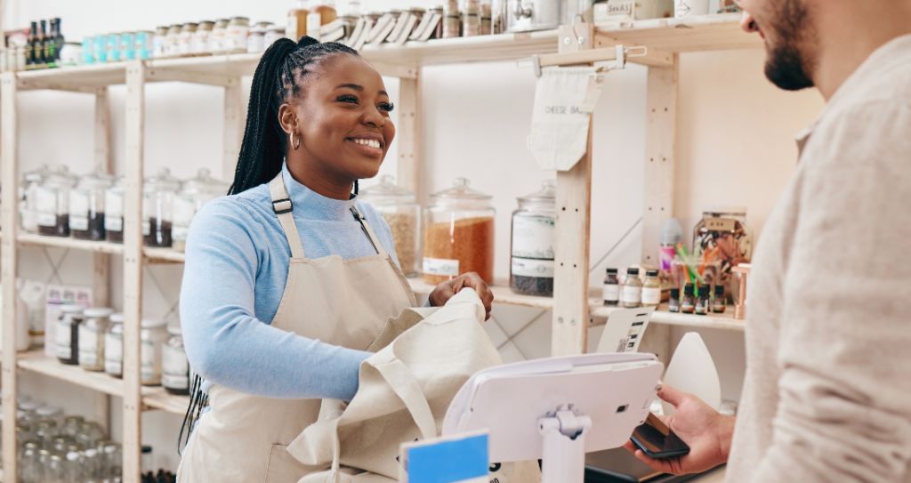 Mulher atendente sorrindo enquanto embala produtos em loja física, ilustrando bom atendimento no Dia do Cliente. 