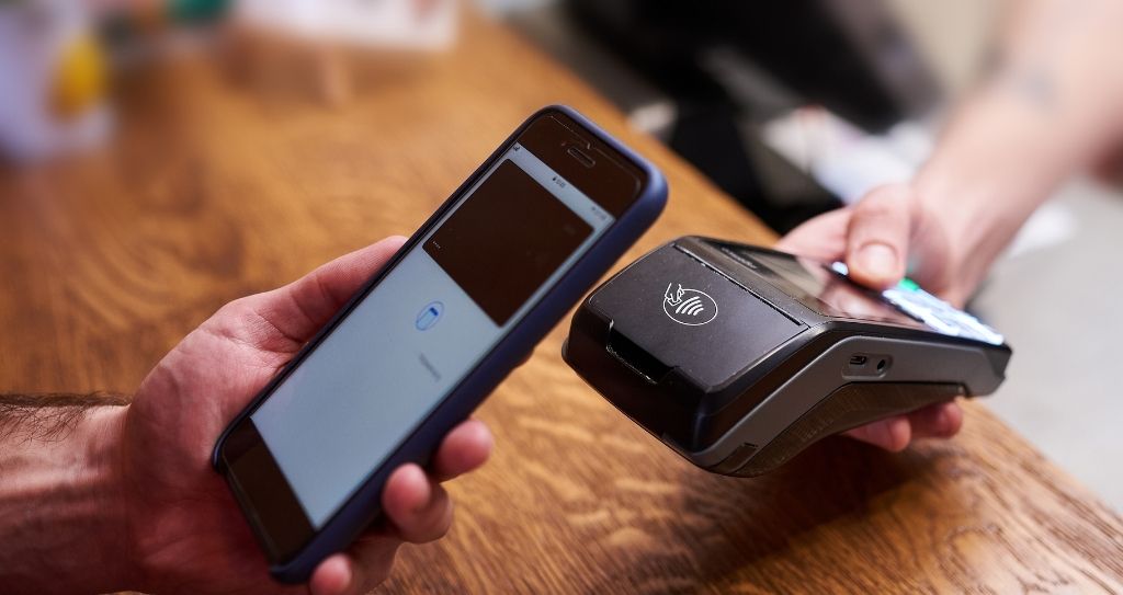 Pessoa realizando pagamento por aproximação com smartphone em maquininha de cartão, ilustrando o que é NFC e sua aplicação em pagamentos móveis.