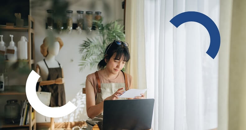 Empreendedora de frente ao seu computador lendo um papel com MEI para vendedor.
