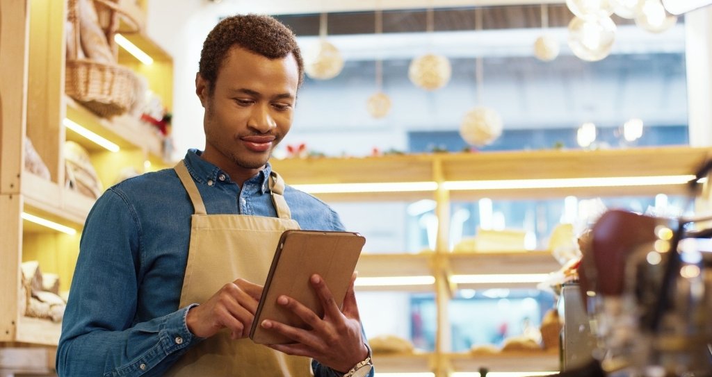 Pessoa empreendedora usando tablet dentro de uma loja, representando o uso da tecnologia na gestão de vendas e precificação. A imagem ilustra a aplicação prática do cálculo de markup e a importância de considerar taxas no valor final dos produtos.