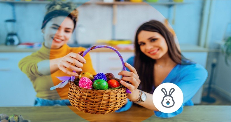 Duas mulheres segurando uma cesta com ovos de Páscoa coloridos, sorrindo.