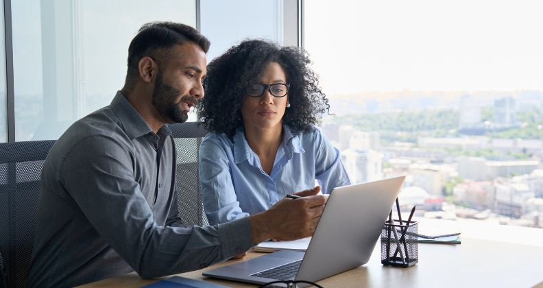 Dois profissionais trabalhando juntos em uma mesa com um laptop em um escritório. 