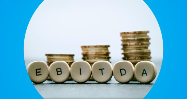 Letras de madeira soletrando EBITDA em frente a pilhas crescentes de moedas com um fundo gradiente azul.