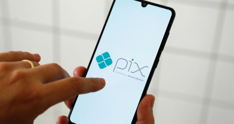 Mão segurando um smartphone exibindo o logotipo do sistema de pagamento “Pix” na tela.