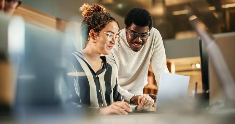 Duas pessoas colaborando na elaboração de documentos de análise financeira em uma mesa em um escritório moderno.