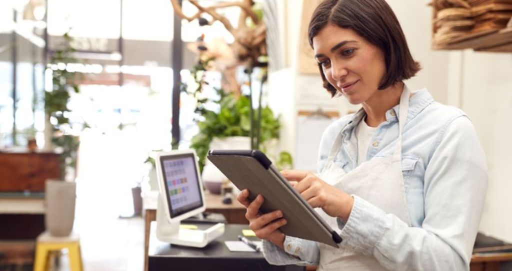 Lojista de avental usando um tablet dentro de uma loja configurando checkout de pagamento online.