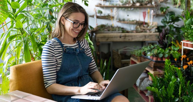 Mulher usando laptop em uma sala cheia de plantas.