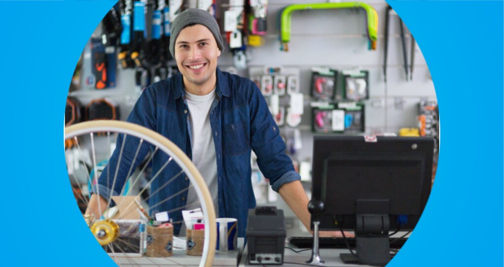 Homem sorridente atrás de um balcão em uma loja de bicicletas e acessórios porque descobriu seu nicho de mercado, possivelmente ele é o dono da loja.