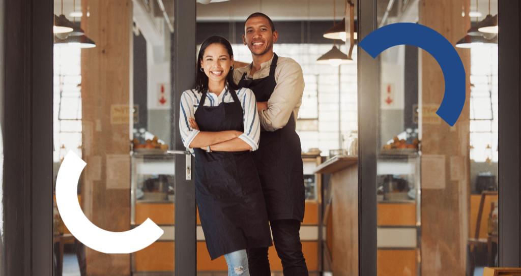 Duas pessoas empreendedoras ME ou EPP, em pé em um café, vestindo aventais, com uma pessoa posando com os braços cruzados.