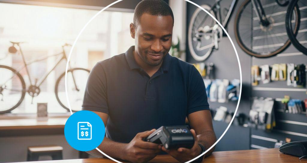 Homem usando a maquininha de pagamento inteligente da Cielo para finalizar o processo de vendas em uma loja de bicicletas, exemplificando a digitalização do processo de vendas no varejo físico.