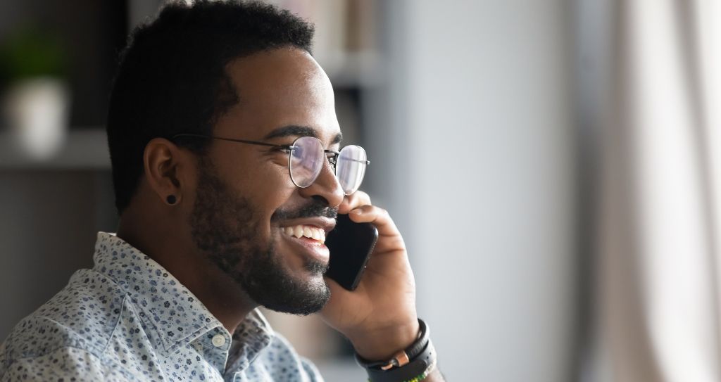 Pessoa segurando um telefone junto ao ouvido, vestindo uma camisa estampada, dentro do escritório, em abordagem a um lead no processo de vendas. 