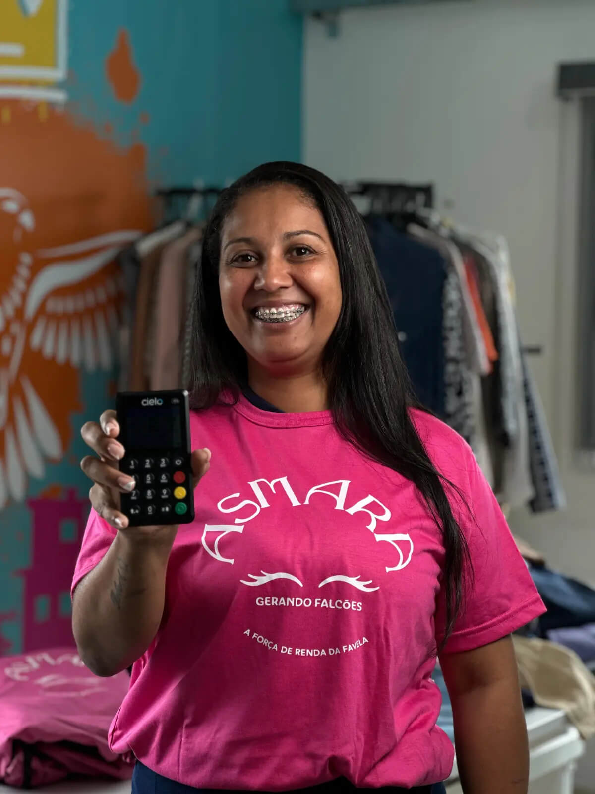 Mulher com camisa rosa do projeto Asmara segura maquininha da Cielo.