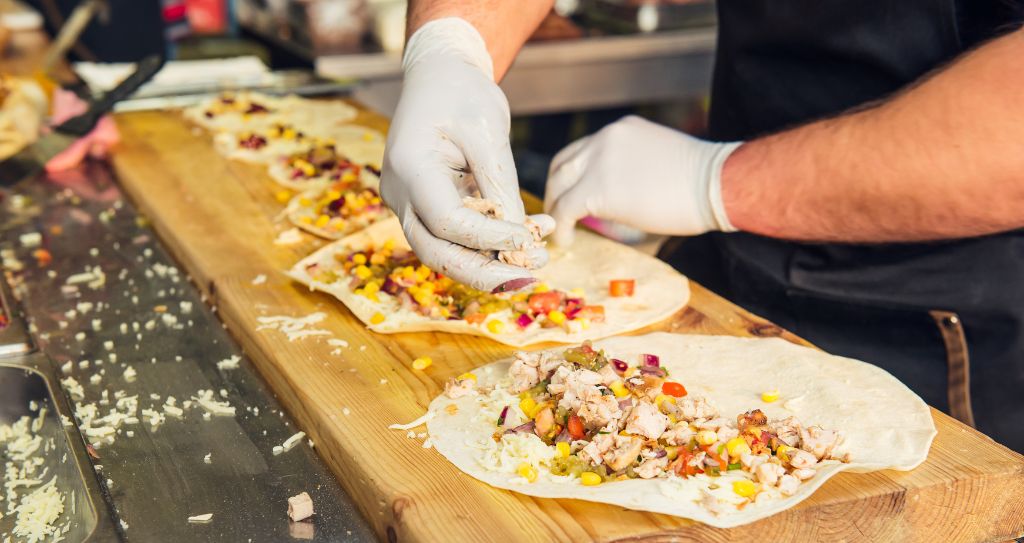 Pessoa desempenhando uma das atividades do MEI, preparando tacos com vários recheios sobre uma superfície de madeira.