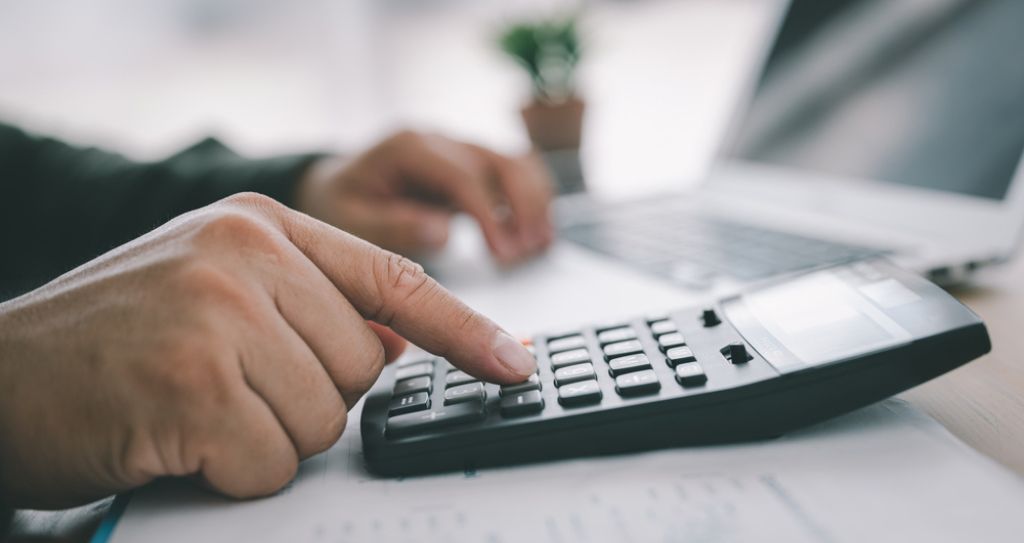 Pessoa usando uma calculadora ao lado de um laptop em uma mesa considerando utilizar split de pagamento. 