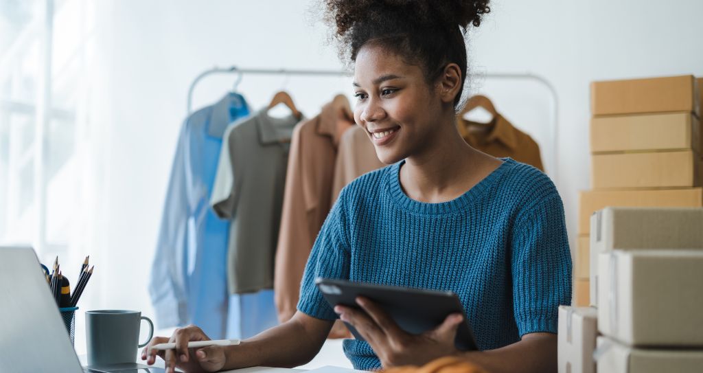 Empreendedora sorridente faz o controle de faturamento do MEI em seu pequeno negócio de roupas.