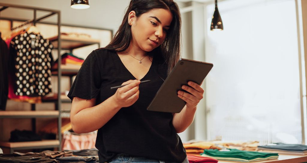 Empresária em loja de moda usando tecnologia para gerenciar o negócio, cenário comum entre quem pesquisa a diferença entre MEI e ME para escolher o enquadramento ideal.
