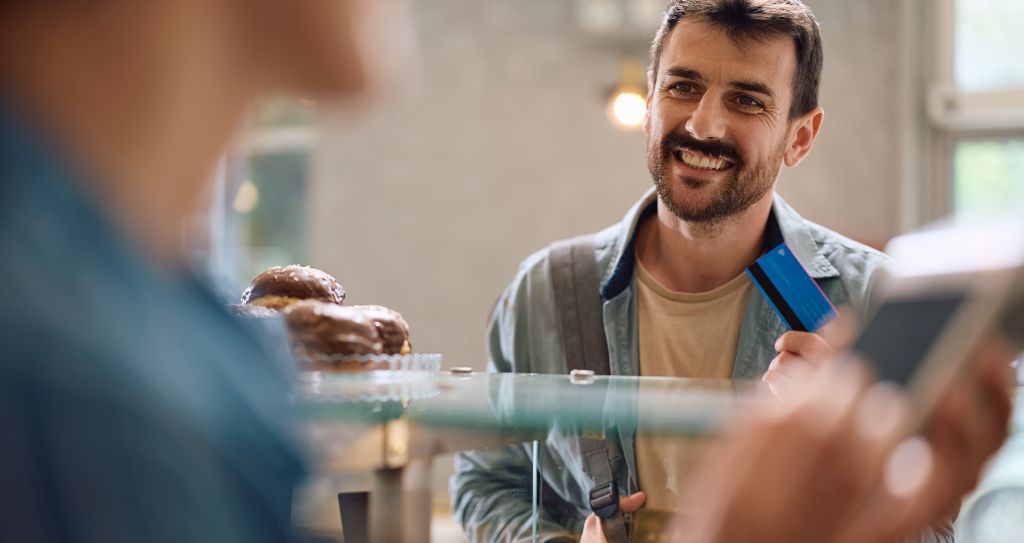 Homem sorrindo enquanto realiza pagamento com cartão, ilustrando a importância de aceitar pagamentos ao empreender e explorar o que vender para ganhar dinheiro.