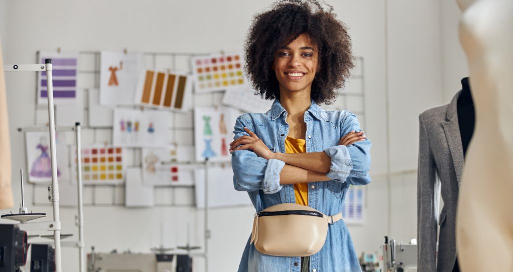 Empreendedora da área de roupas e acessórios posando em seu ateliê, representando ideias de o que vender para ganhar dinheiro com moda e personalização.