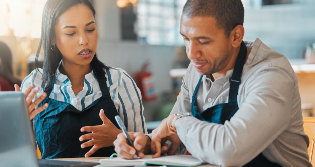 Duas pessoas sócias de um café conversando e fazendo anotações sobre gestão financeira empresarial, simbolizando o planejamento e a tomada de decisão com base em dados.