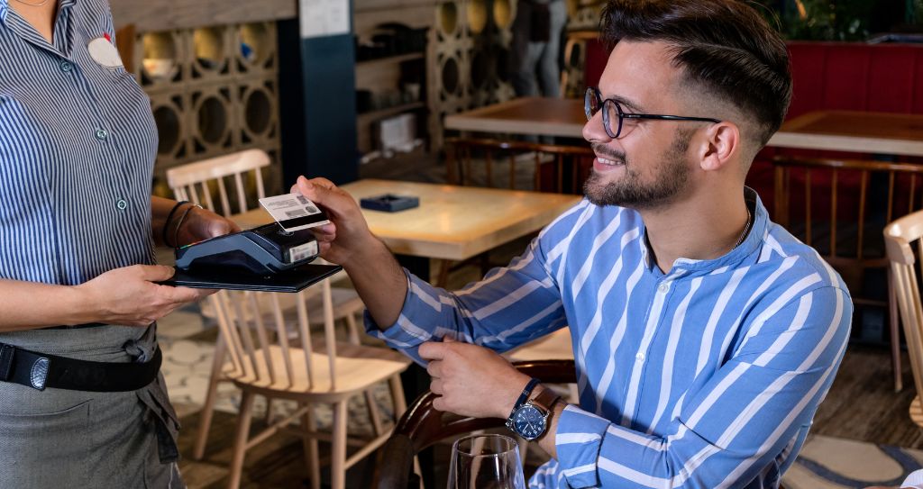Cliente realizando pagamento por aproximação com cartão em maquininha Cielo ao finalizar a conta em restaurante