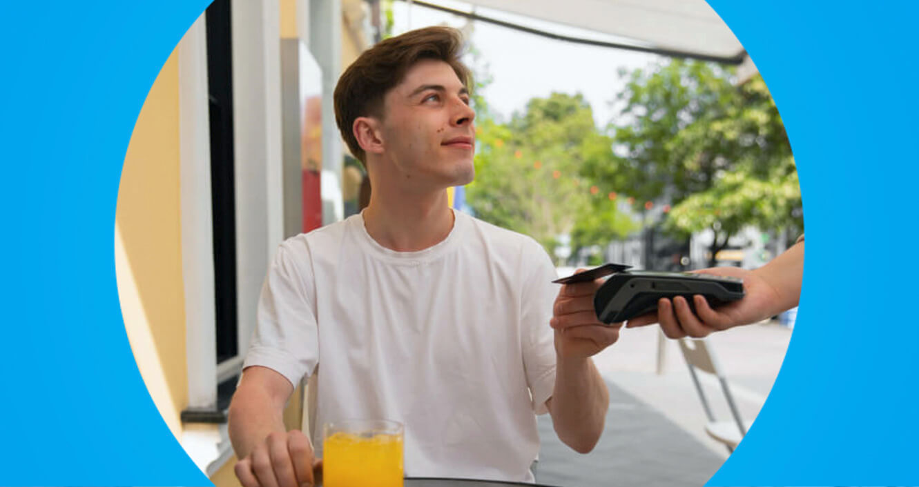 Cliente pagando com cartão em maquininha na mesa de restaurante ao ar livre.