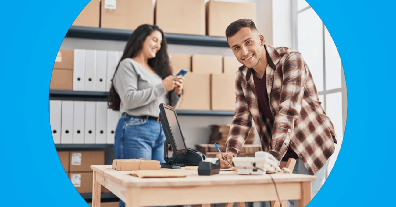 Dois empreendedores em depósito organizando pedidos, com maquininha de cartão sobre a mesa