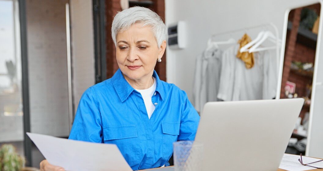 Empreendedora com papel na não e notebook faz cálculo de taxa mdr.