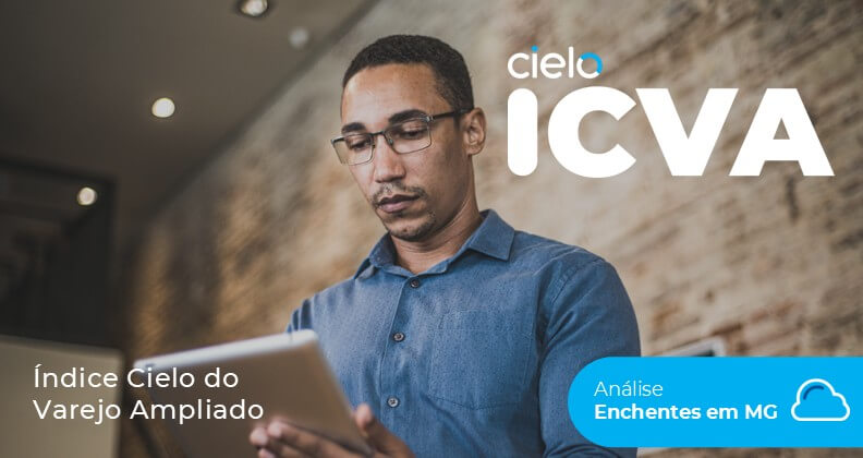 Empreendedor com semblante preocupado, utilizando um tablet em ambiente interno de um estabelecimento, enquanto analisa dados do Índice Cielo do Varejo Ampliado (ICVA). A imagem destaca estudo sobre o impacto das enchentes em Minas Gerais, com referência à marca Cielo e à análise de vendas do varejo no estado.