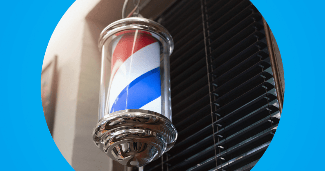 poste giratório de barbearia com listras vermelhas, brancas e azuis fixado na fachada.