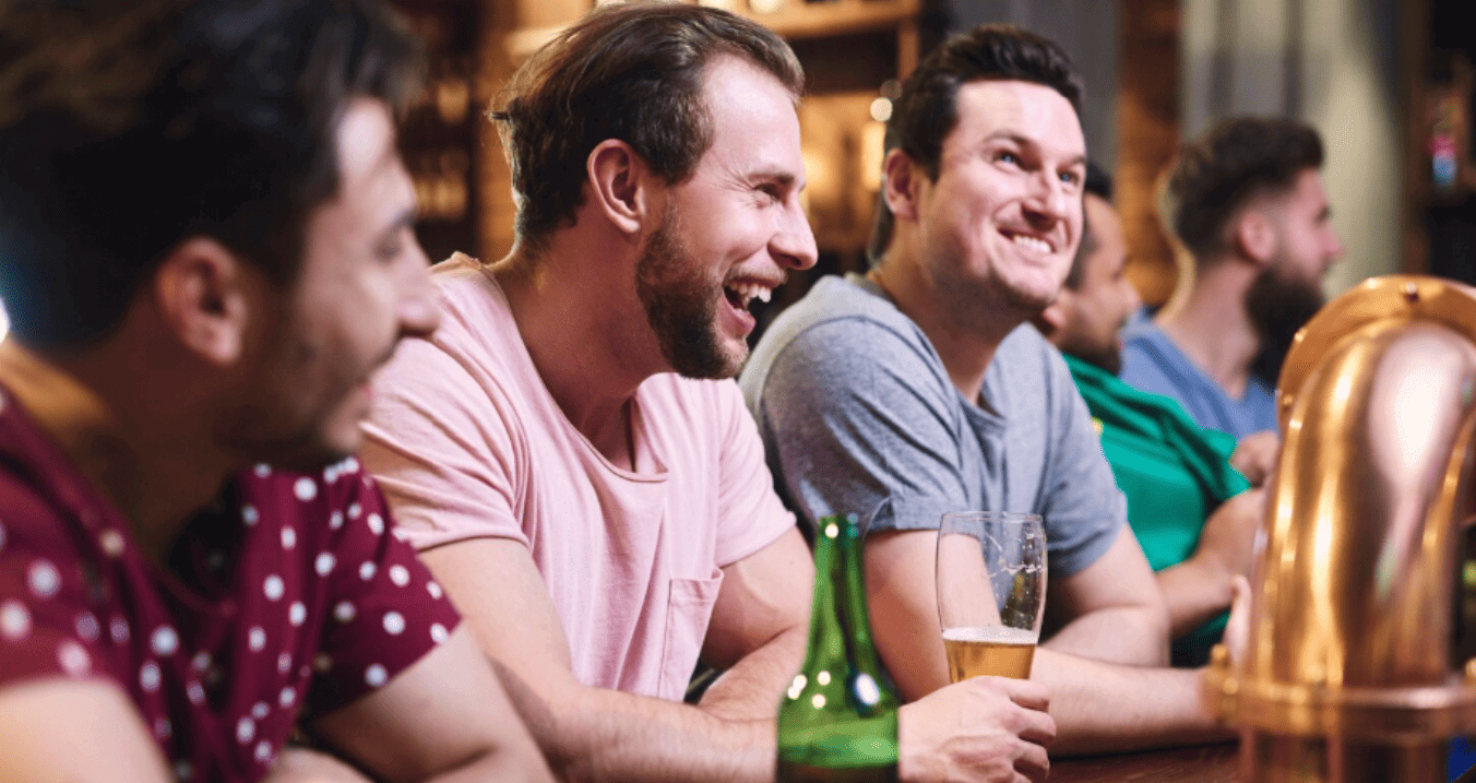 grupo de amigos sorridentes com cervejas no balcão de um bar iluminado.