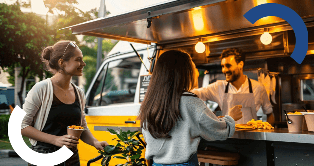 Um homem e uma mulher estão em frente a um food truck, avaliando as opções de comida disponíveis.