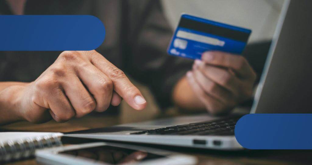 Detalhe de mãos de pessoa segurando cartão de crédito enquanto realiza pagamento por cobrança recorrente.