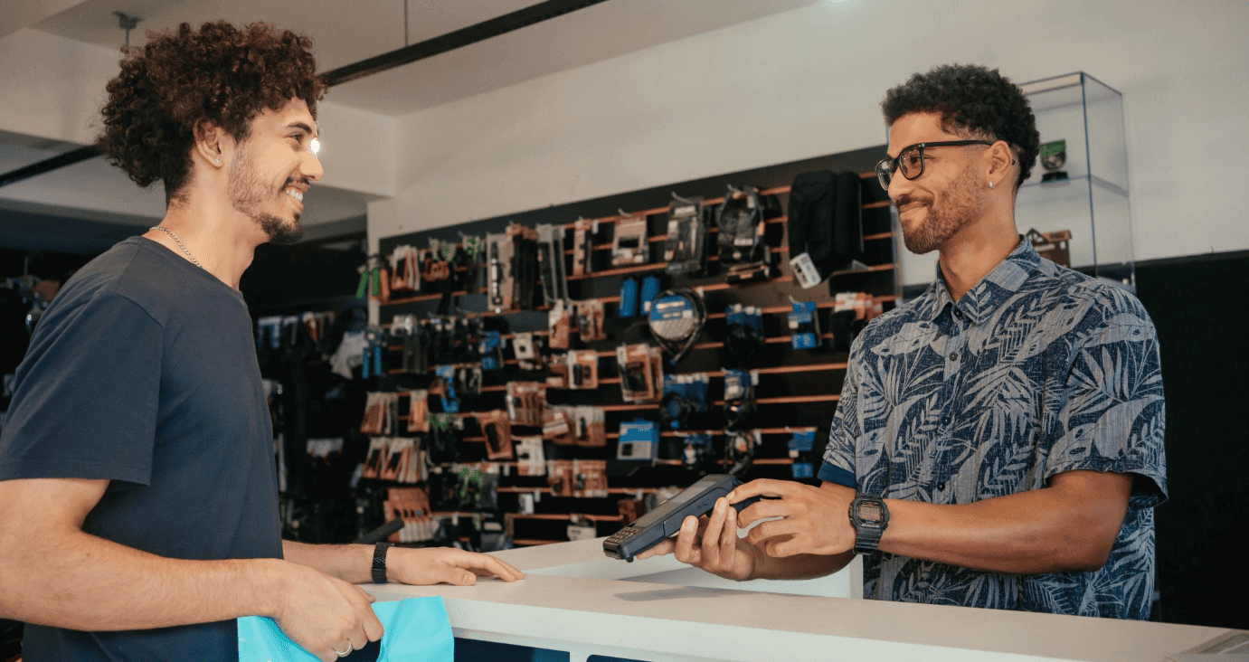 Empreendedor em sua loja recebendo o pagamento de um cliente com sua maquininha Cielo.