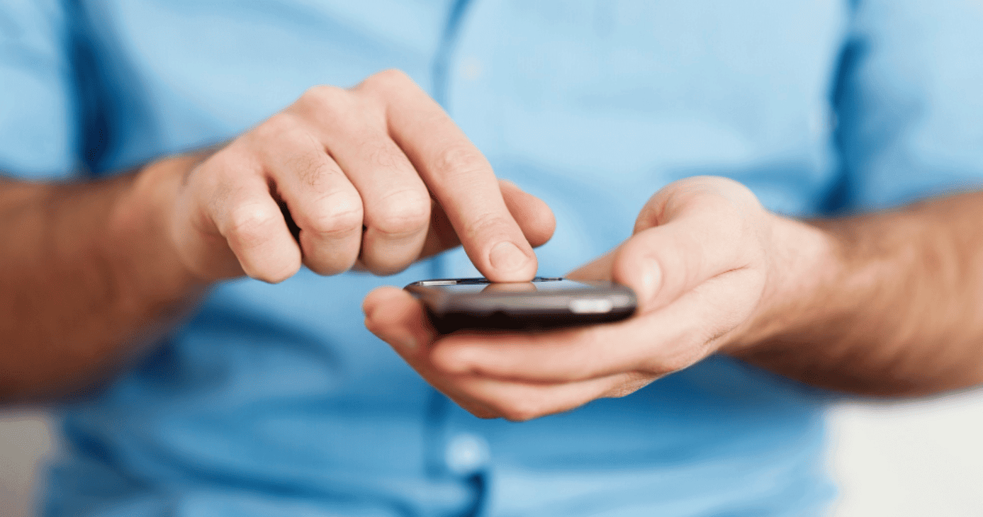 Mãos de um empreendedor mexendo em um celular, fazendo pagamento invisível.