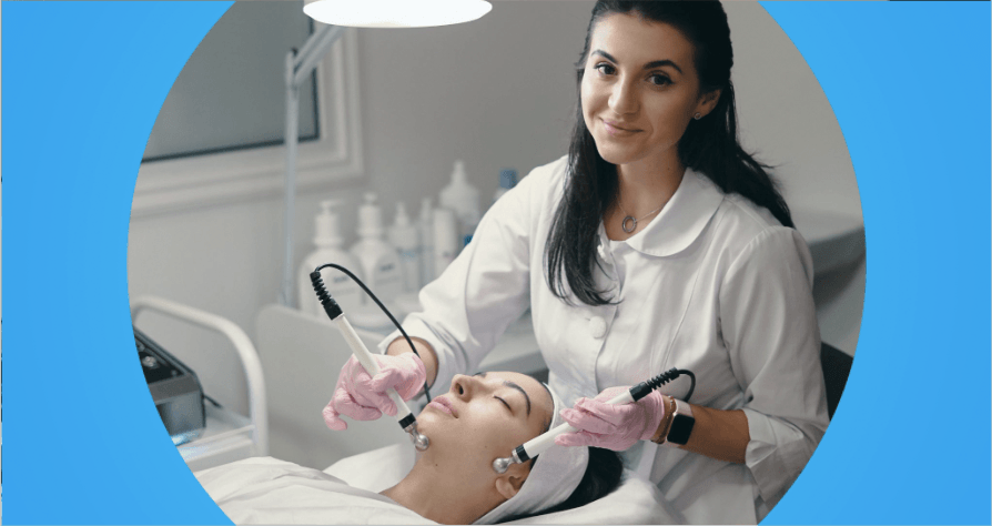 esteticista com jaleco branco realiza procedimento facial com equipamentos em cliente deitada na maca.