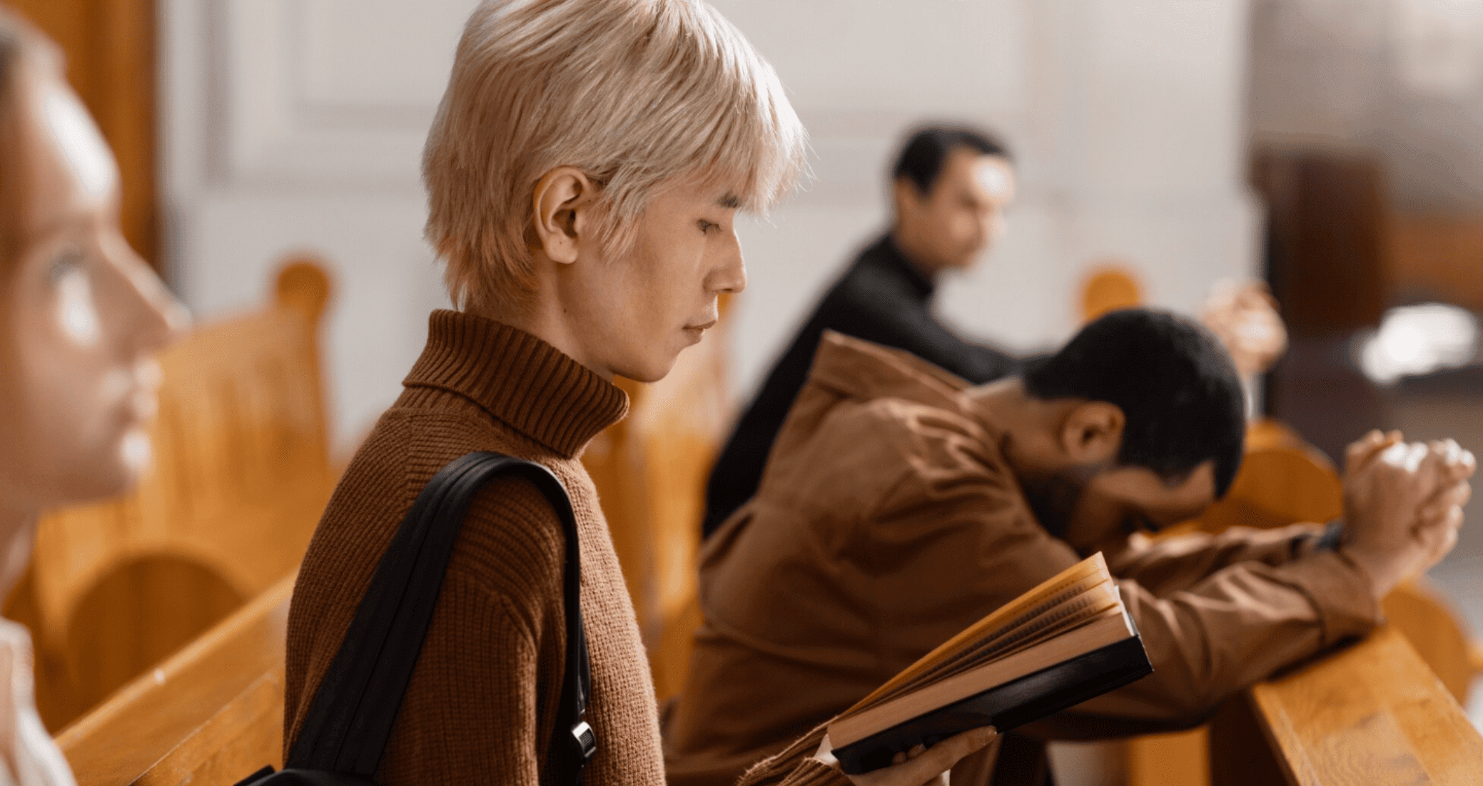 fiéis sentados em bancos de igreja durante culto, um deles com livro aberto nas mãos.