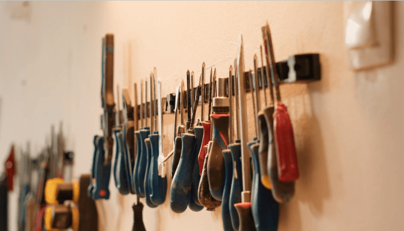 Uma parede com diversas ferramentas abertas, incluindo martelos, chaves e alicates organizados de forma ordenada.
