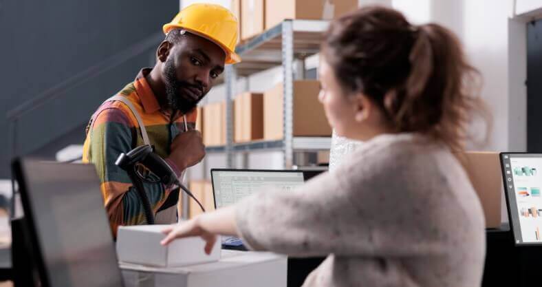 Um homem e uma mulher num espaço de armazém, com várias caixas ao fundo.